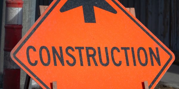 Orange diamond shaped road construction sign with a black arrow pointing ahead at a street site.